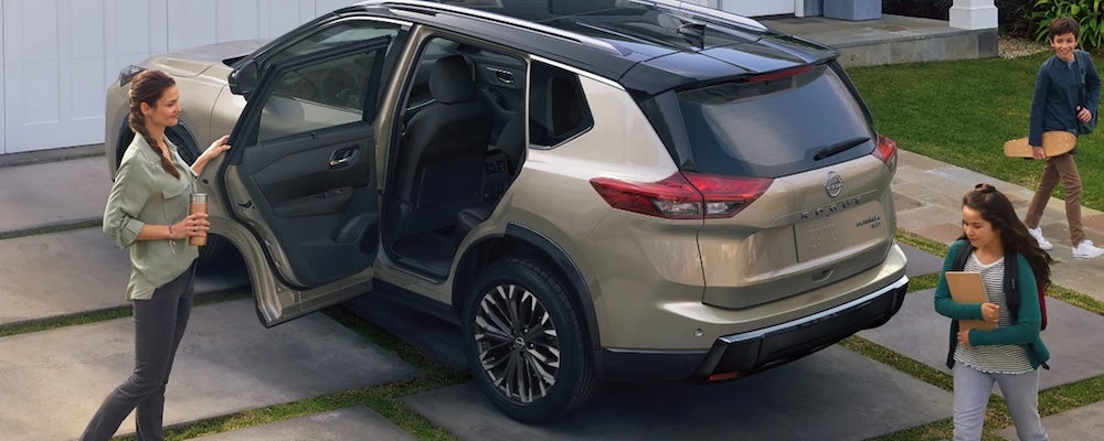A family walking near a beige 2026 Nissan Rogue SUV parked in their driveway