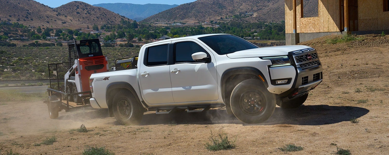 A white Nissan Frontier driving off-road while towing a trailer