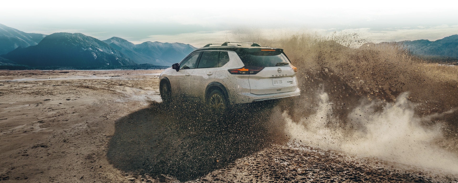 A white Nissan Rogue kicking up heavy dirt as it drives off-road