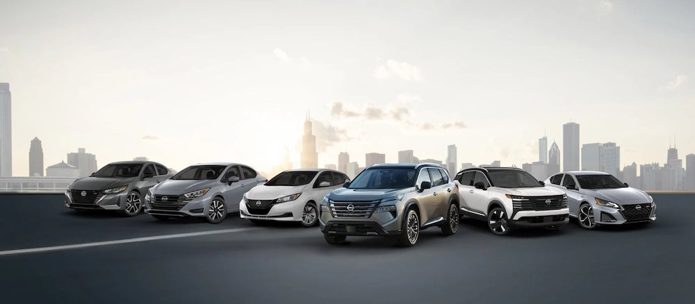 Several Nissan sedans ans SUVs parked together with a city in the distance
