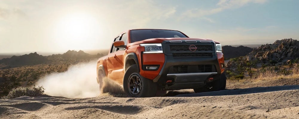 An orange 2026 Nissan Frontier pickup truck driving up a sandy incline