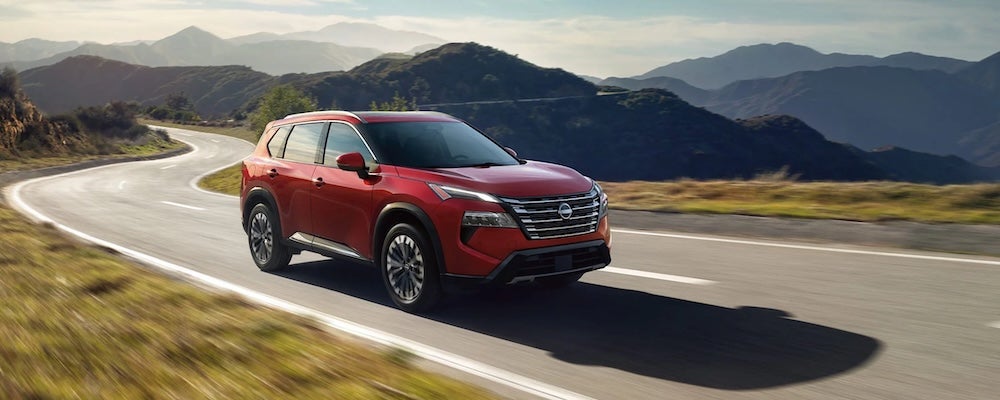 A red 2026 Nissan Rogue SUV driving down a winding road