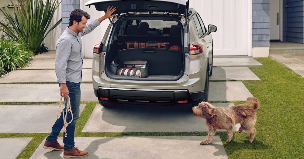 A man and his dog at the open trunk of a beige Nissan Rogue SUV